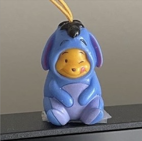 A Peek A Pooh charm of Winnie the Pooh dressed up as Eeyore, resting on top of a desktop monitor.